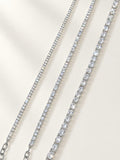 Three tennis-style necklaces with clear stones in silver-toned settings, arranged diagonally on a light cream background.